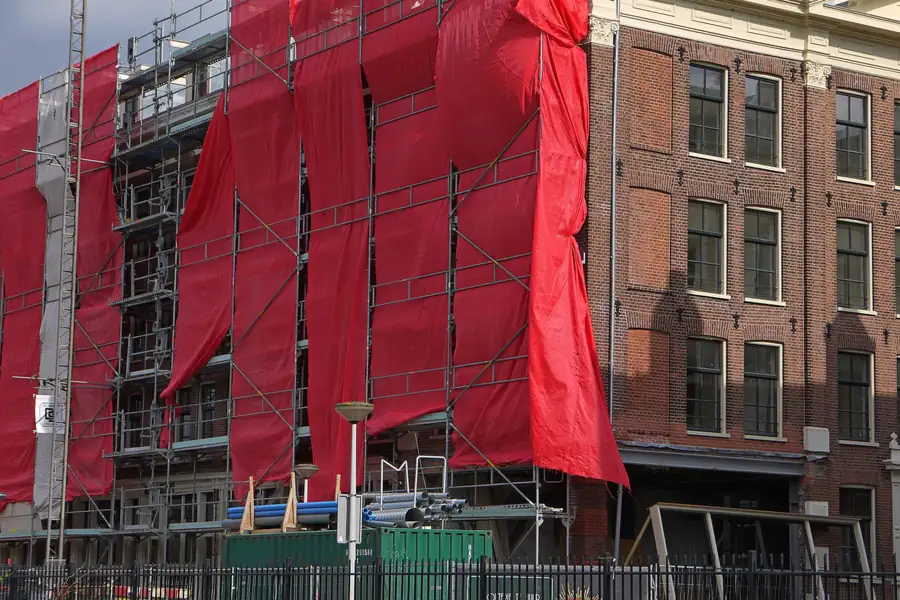 Steiger met rode doeken tegen een historisch bakstenen pand in Amsterdam tijdens een renovatie