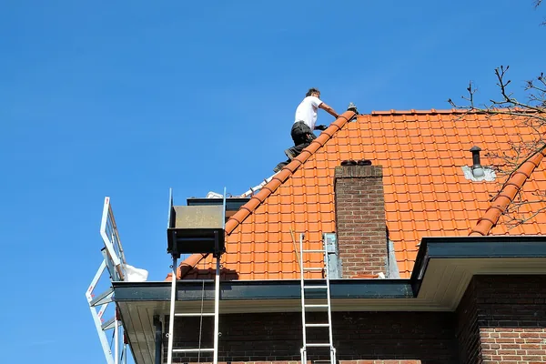Dakdekker op de nok van een pannendak, daklekkage verhelpen in Amsterdam